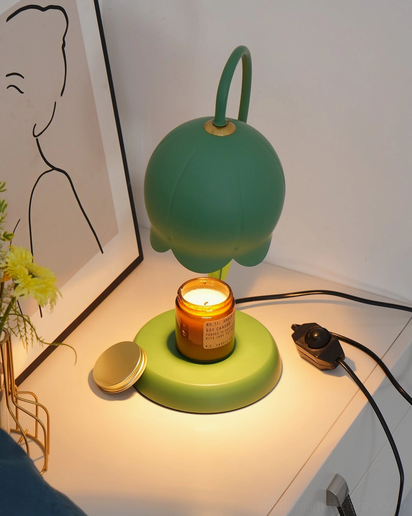 Low frontal view of matte dark green lily candle warmer lamp on bedroom dresser with plant decor and power cord