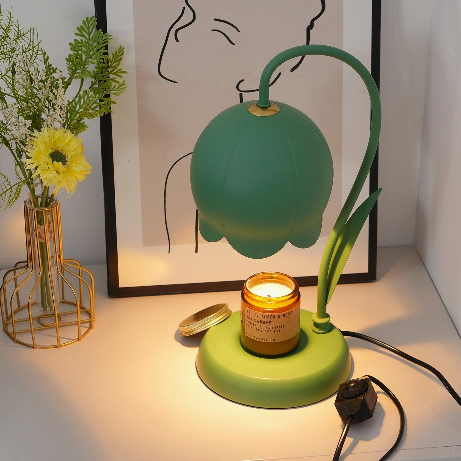 Dark green lily warmer lamp side rear angle view on dresser with minimalist wall art and lit scented candle