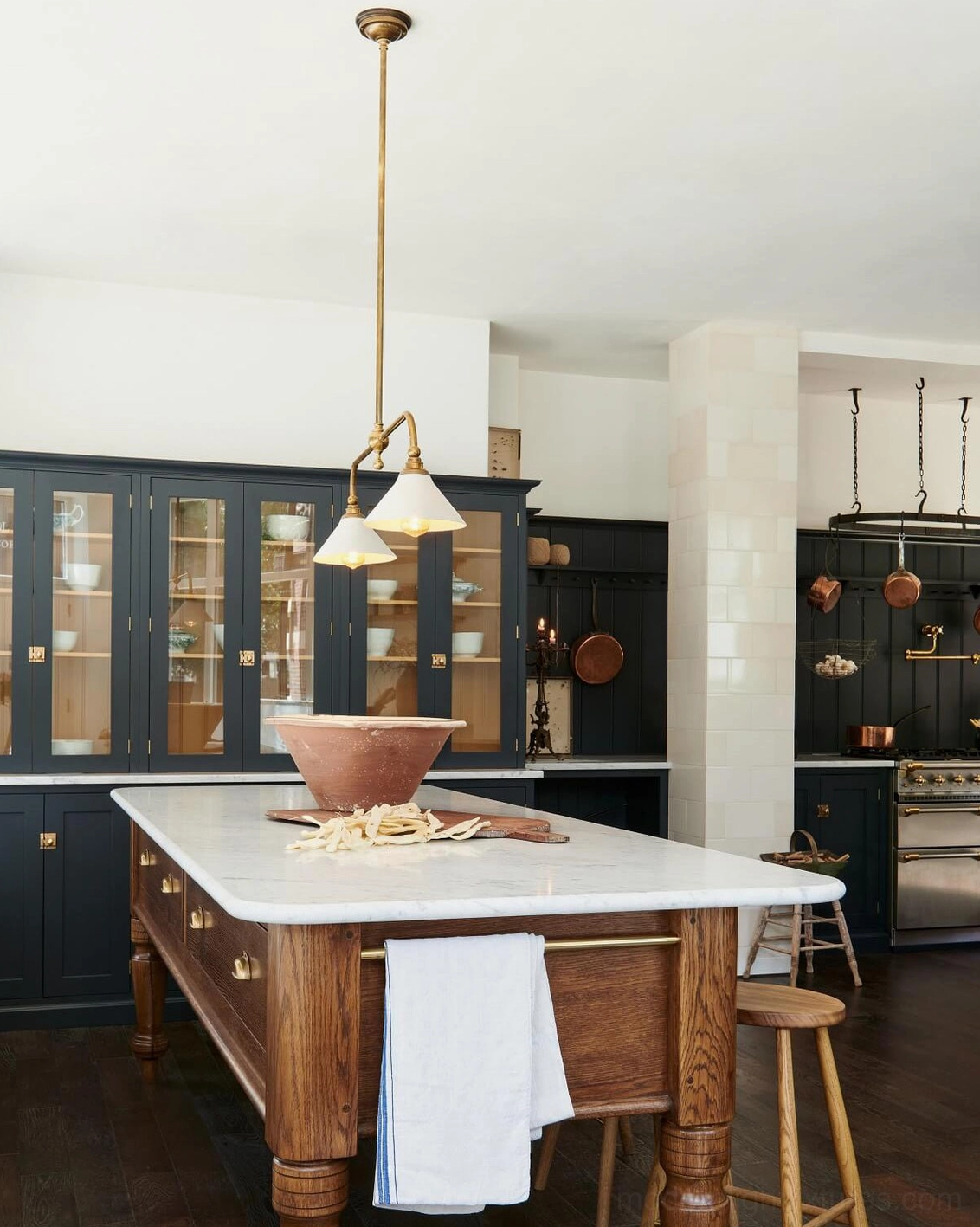 Two-light brass linear pendant with white ceramic shades suspended in warm traditional kitchen with dark blue cabinetry