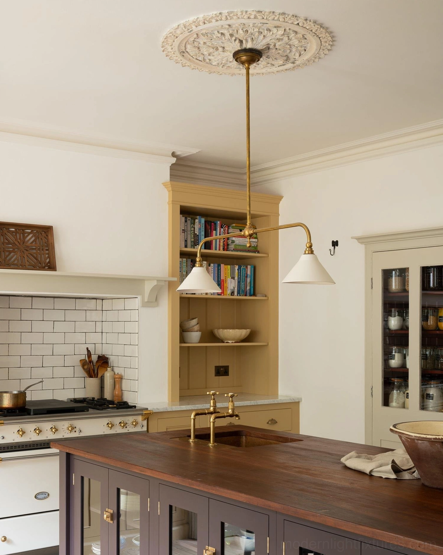 Brass metal frame pendant chandelier with off-white shades installed in bright neutral traditional kitchen with wooden cabinetry