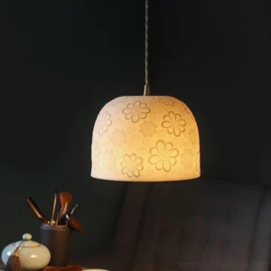 Illuminated ceramic pendant lamp casting warm ambient light, showcasing embossed flower pattern, hanging in contemporary interior with dark green wall