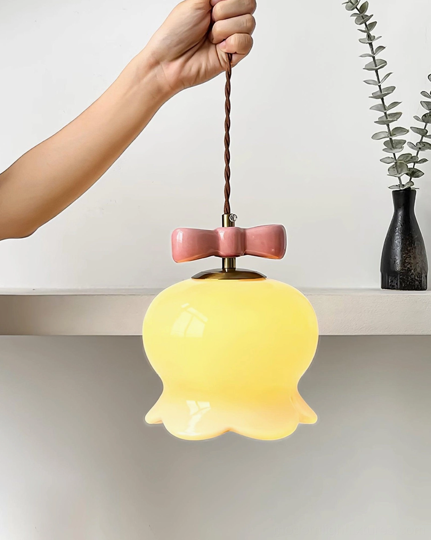 Lit cream ceramic bellflower pendant light with pink bow ornament on minimalist home shelf