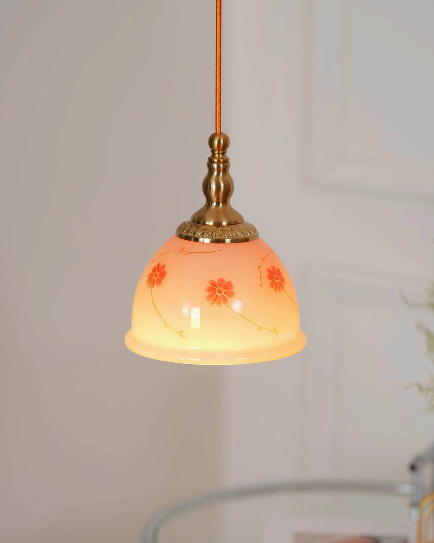 Illuminated ceramic floral pendant light glowing warm amber, displaying brass fixtures and hand-painted flowers