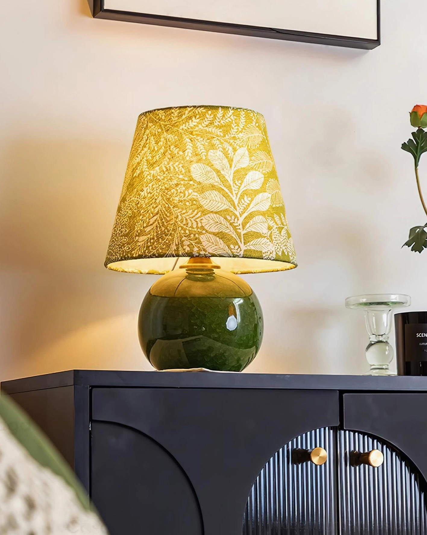 Illuminated green ceramic table lamp with warm light, three-quarter view on dark wood surface