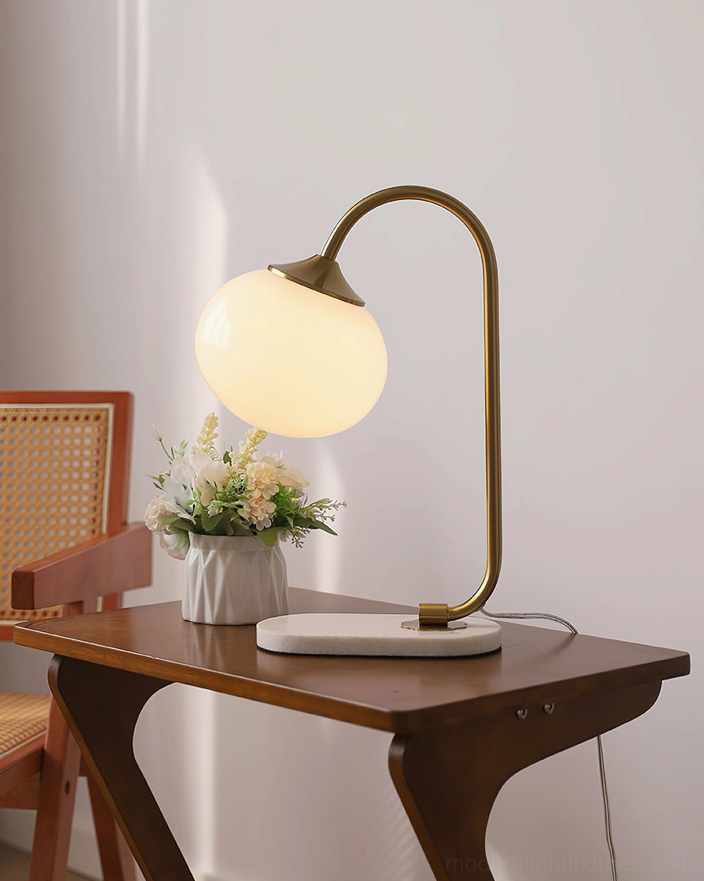 Lit pink glass globe table lamp emitting warm white light with brass gold frame and marble base in bedroom setting