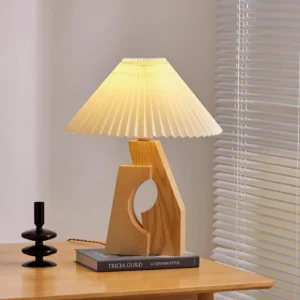 Illuminated pleated table lamp with natural wood base on home office desk, warm soft glow with window blinds background