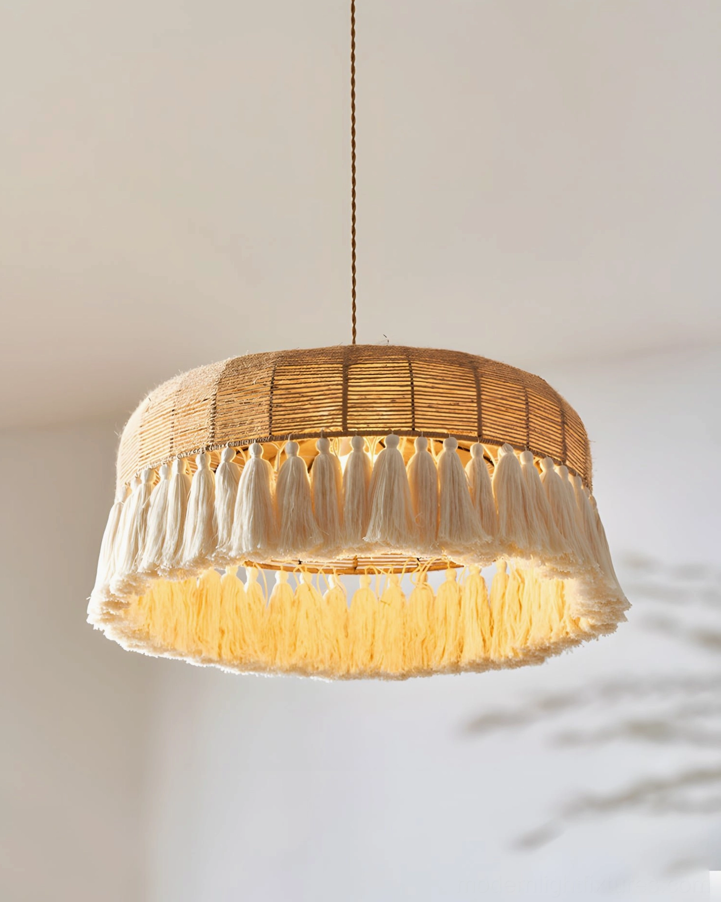 Lit woven rattan tassel pendant light with warm amber glow, close-up detail of natural hemp rope weave and white fringe