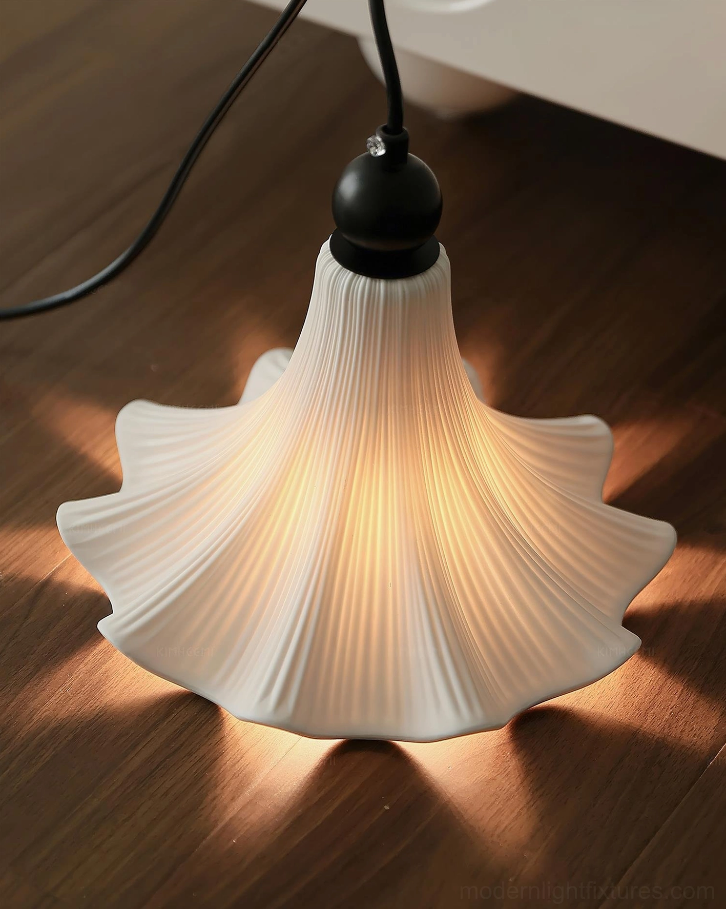 Illuminated Florin Ripple pleated ceramic pendant light casting warm glow with black twisted cord, wooden floor tabletop scene
