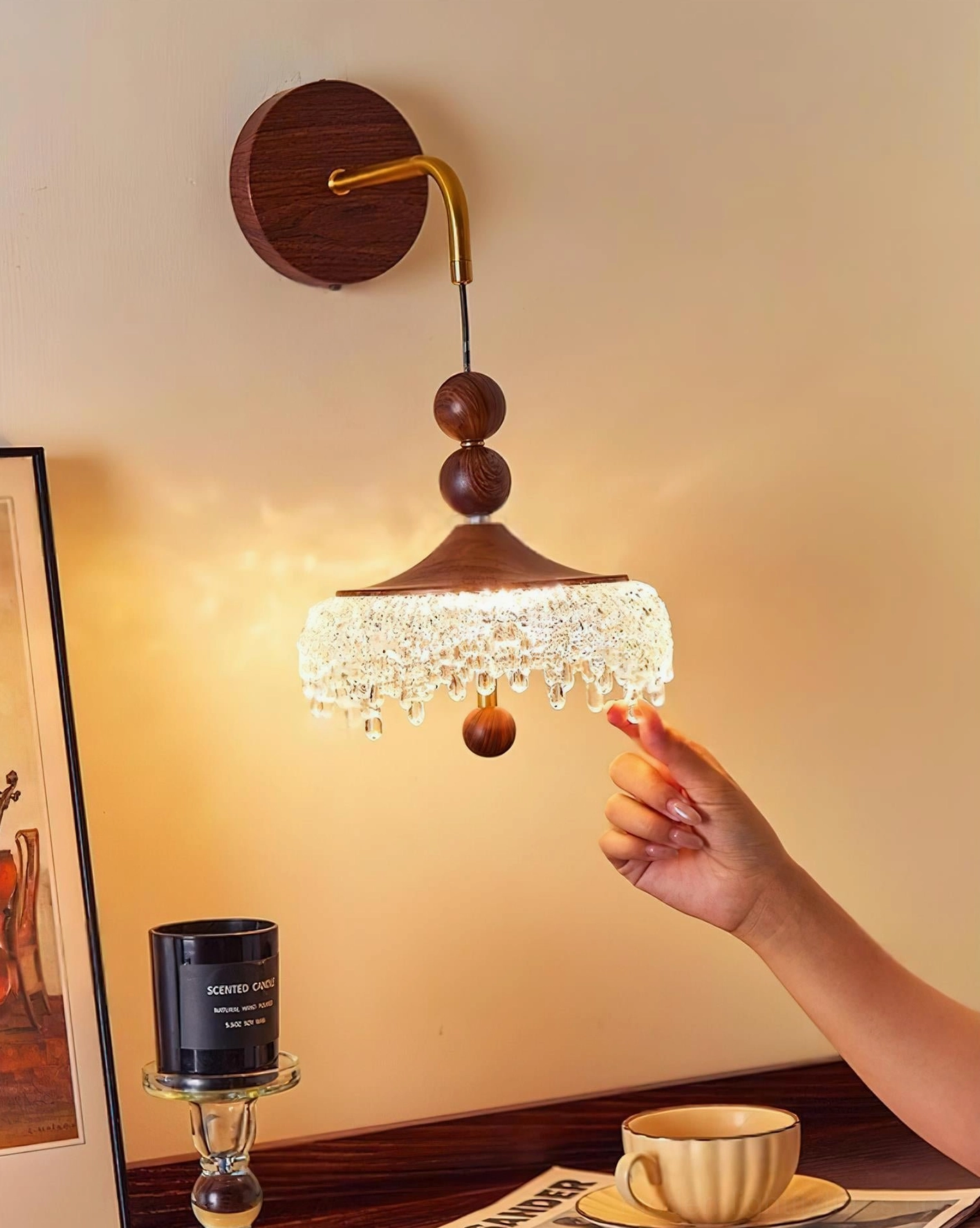 Illuminated crystal wall sconce with hand interaction at wooden bead detail showing product scale and craftsmanship