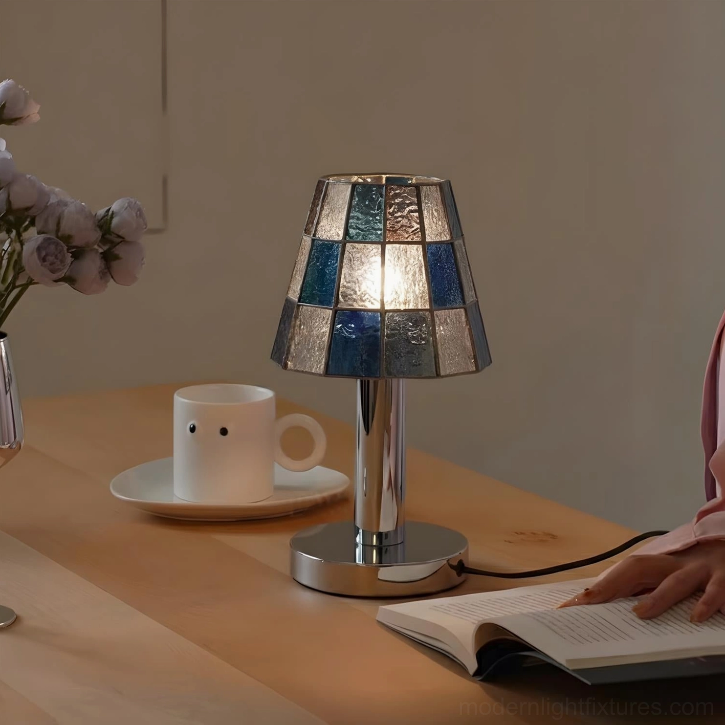 Contemporary geometric glass table lamp with blue tiles illuminated on home dining table with coffee and book