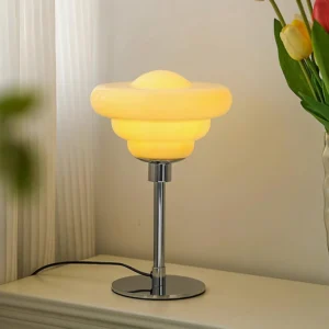 Illuminated creamy yellow retro tiered table lamp on bedroom dresser with glass tulip vase and floral decor