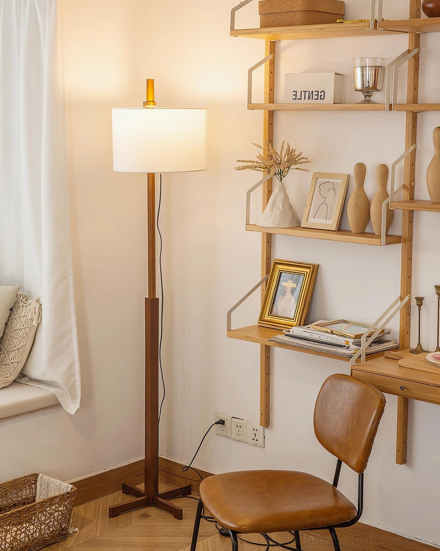 Illuminated modern walnut floor lamp with warm glowing white fabric shade in evening home workspace setting