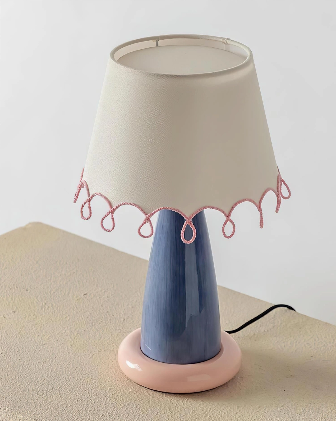 Lollio ceramic table lamp with blue stem and pink base, three-quarter view showing fabric shade and visible power cord