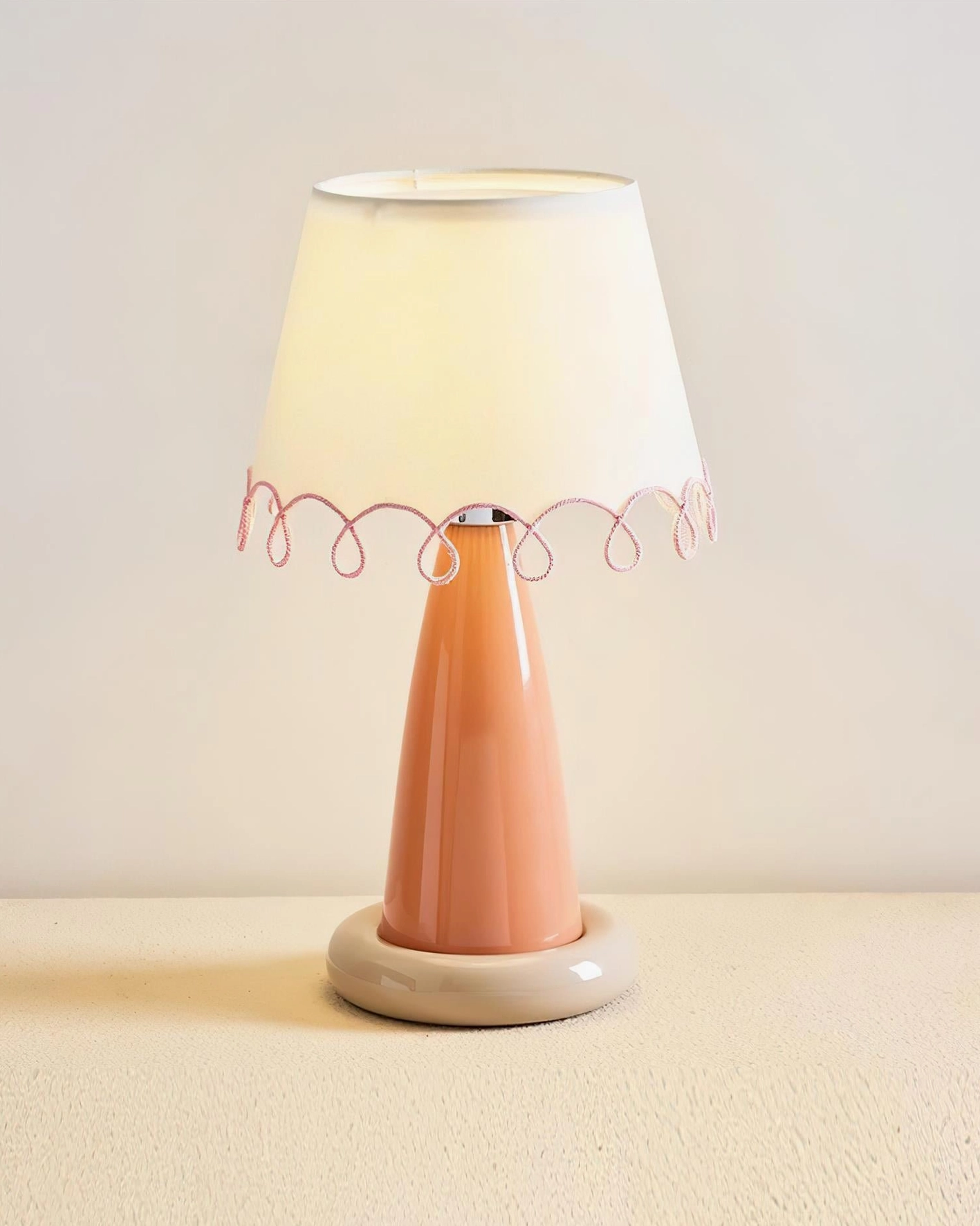 Lollio ceramic table lamp with terracotta orange stem and beige base, illuminated on beige tabletop studio setting