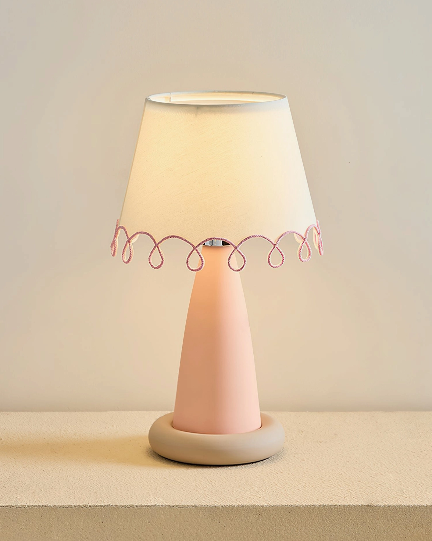 Lollio ceramic table lamp with pale pink stem and beige base, front low-angle view with white shade and pink scalloped trim