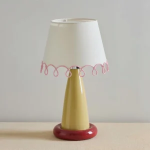 Lollio modern ceramic table lamp in red and yellow color combination, unlit on beige tabletop with contemporary studio styling