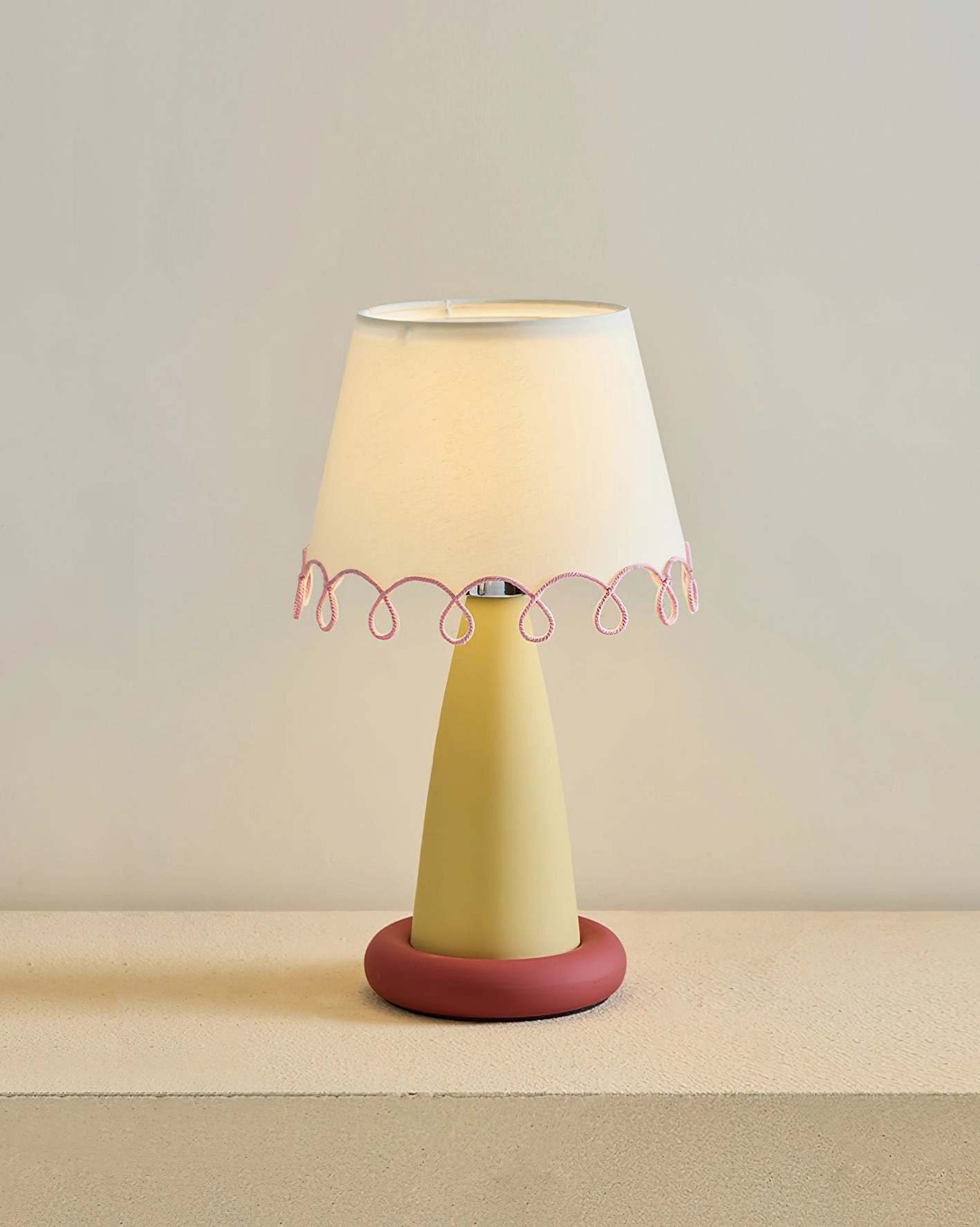 Lollio table lamp variant with yellow ceramic stem, red round base, and white fabric shade with pink loop trim detail