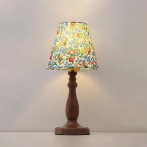 Illuminated Lottie botanical print table lamp on gray surface, warm ambient lighting, floral fabric shade