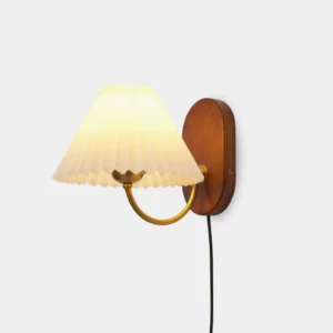 Louise plug-in wall sconce with pleated fabric shade, front studio view showing ash wood backplate and brass arm
