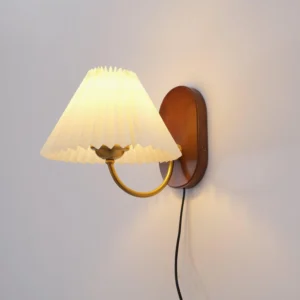 Louise plug-in wall lamp three-quarter angle displaying oval wood mount, brass curved arm, and folded fabric shade
