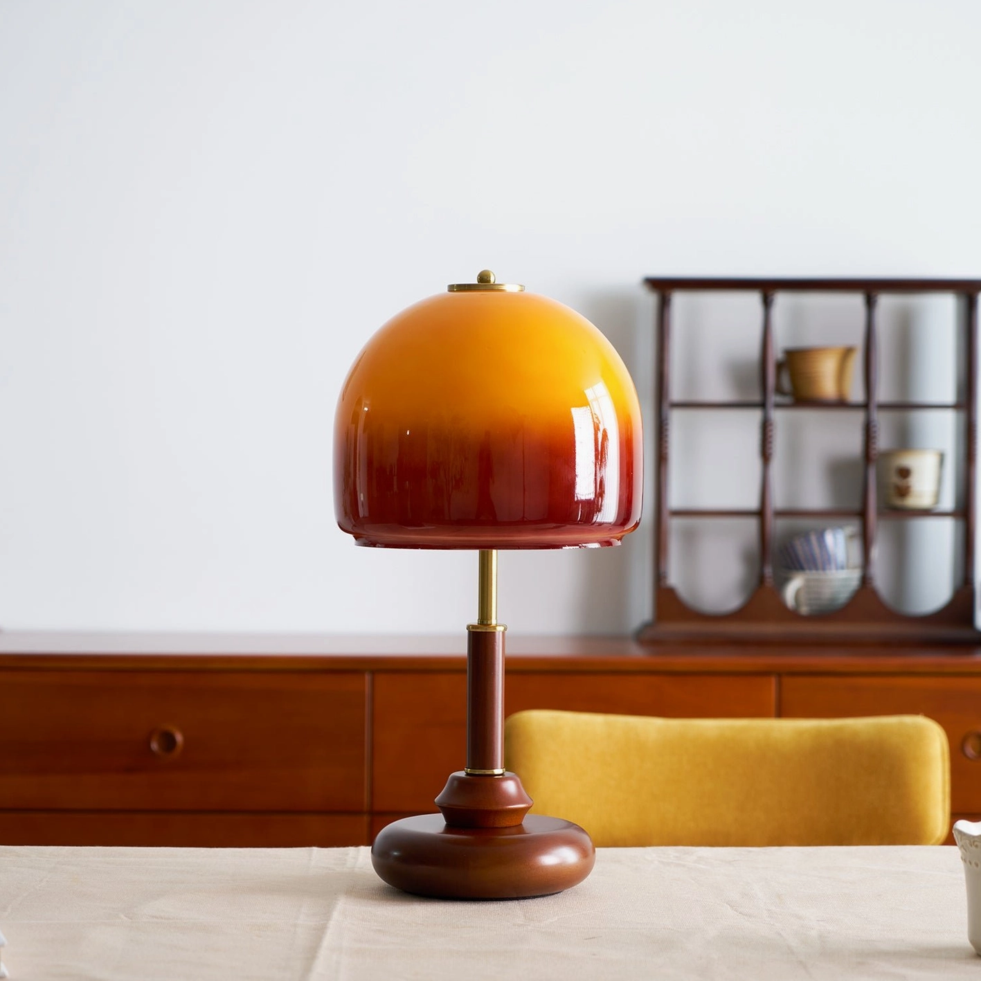 Luciano table lamp in dining room with yellow upholstered chair and wall-mounted wooden shelf, contemporary setting