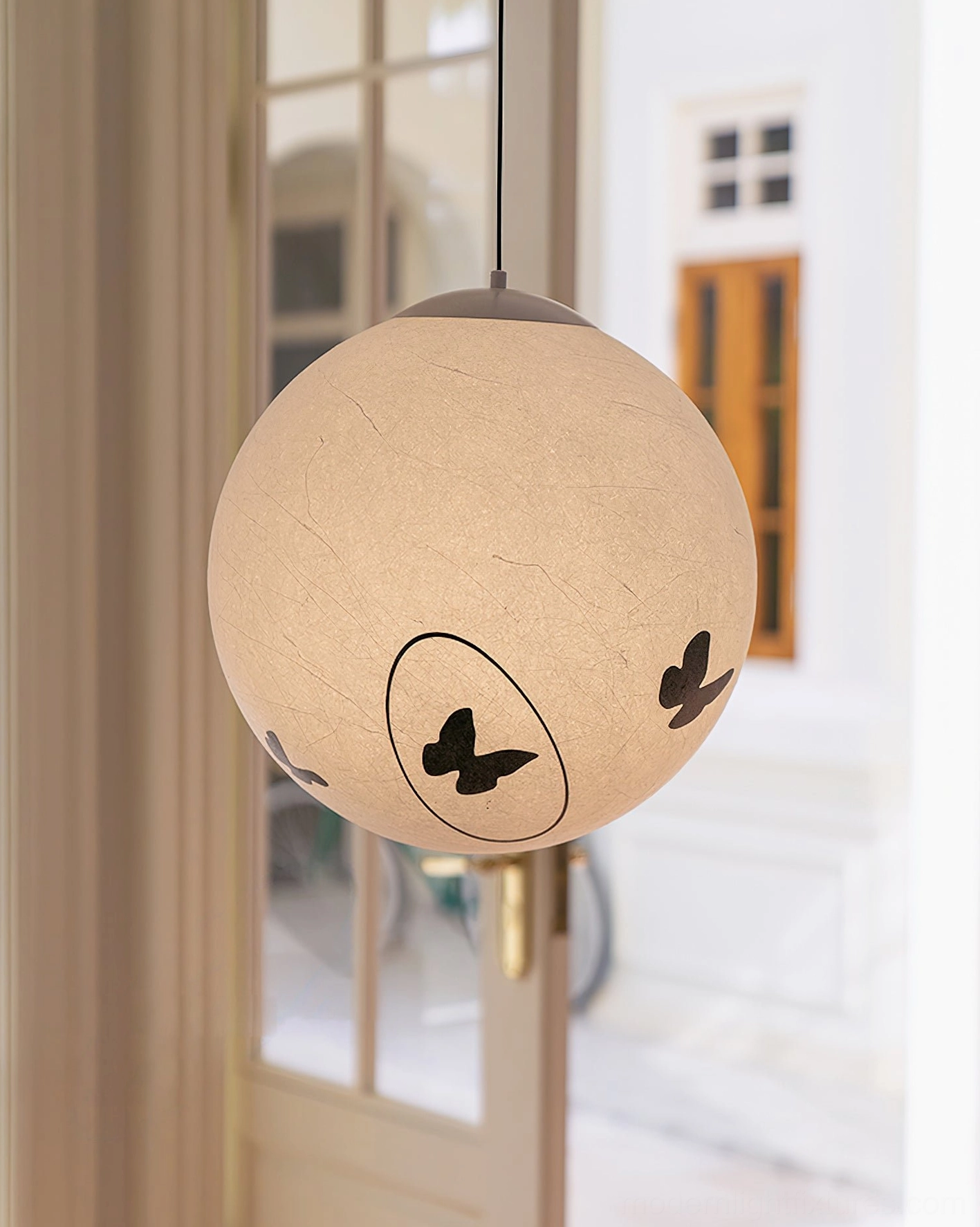 Luna Flutter butterfly pendant lamp lit in entryway setting, warm beige textured shade with black butterfly motifs glowing
