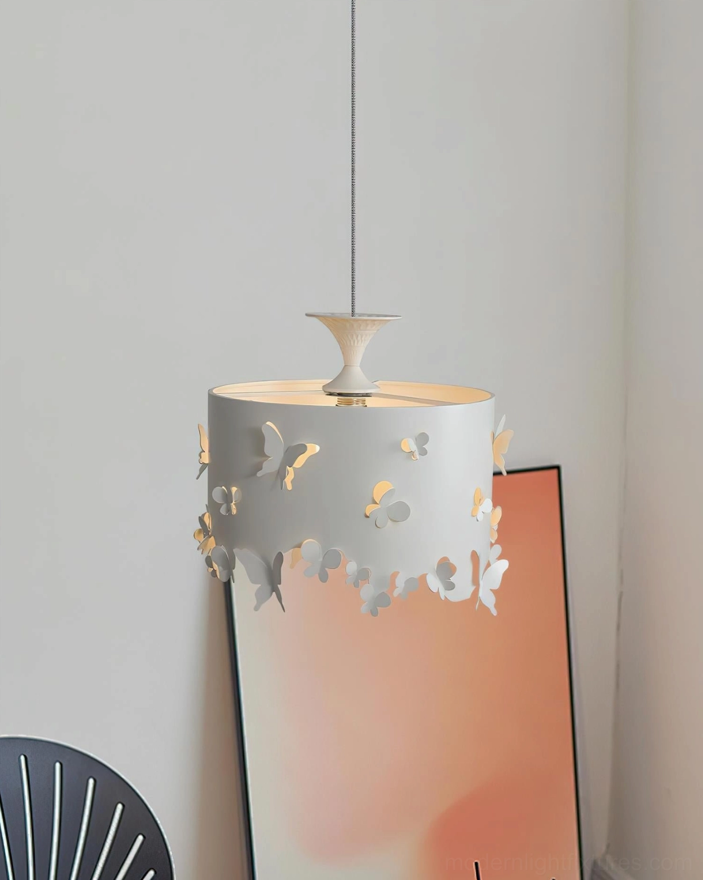 Modern pendant lamp with butterfly shade installed above minimalist black accent chair in living room corner with gradient wall art