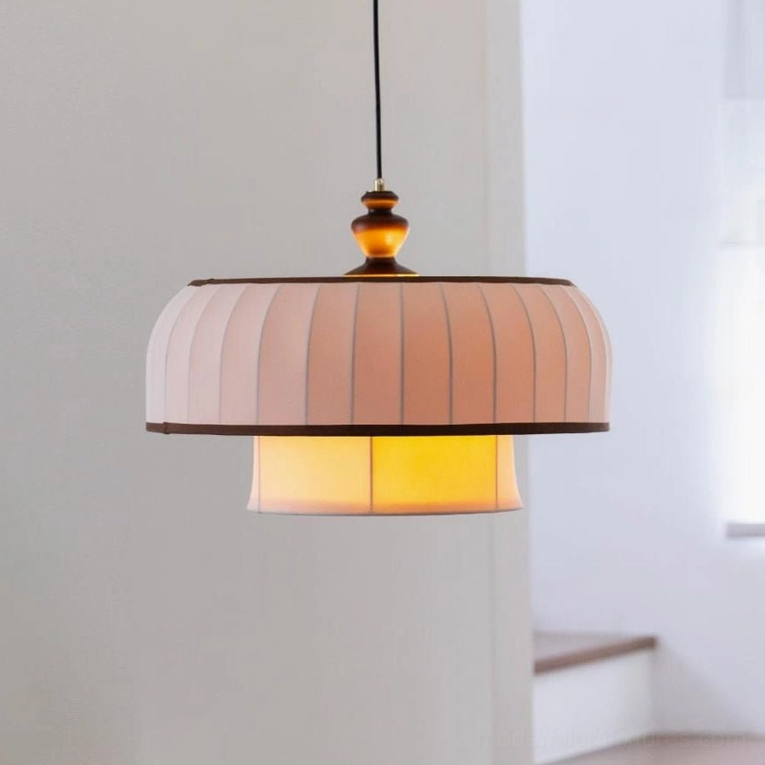 Front close-up view of Lunette pendant lighting the two-tier pleated fabric construction, dark piping detail, and warm interior glow through lower tier