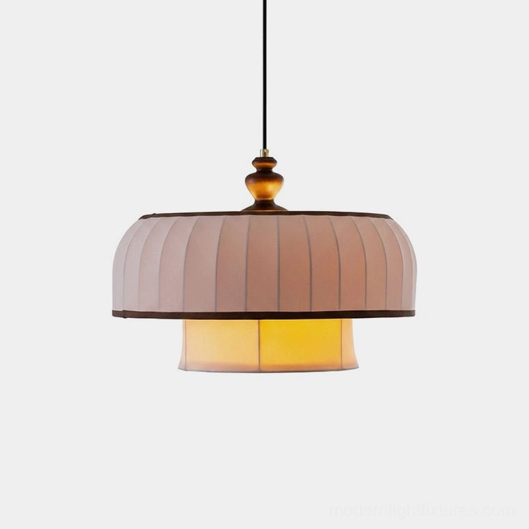Lunette two-tier pleated fabric pendant light with turned wood finial, suspended low, showing warm cream pleated shade with dark walnut contrast piping trim and internal warm light glow