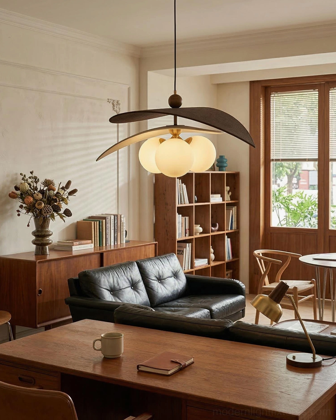 Lunova modern pendant light mounted above wooden study desk in home office with leather sofa, side view of sculptural fixture
