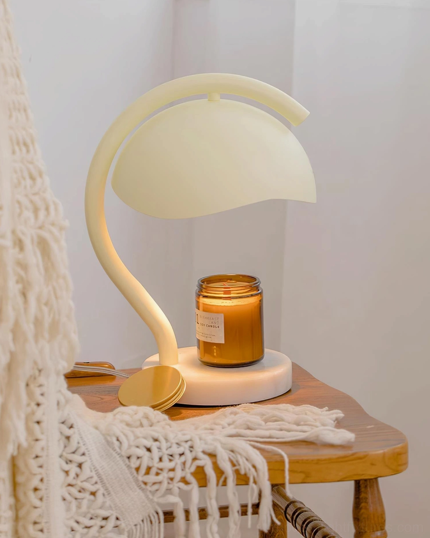 Contemporary alabaster candle warmer lamp with jarred scented candle and brass lid on wooden side table with knitted throw