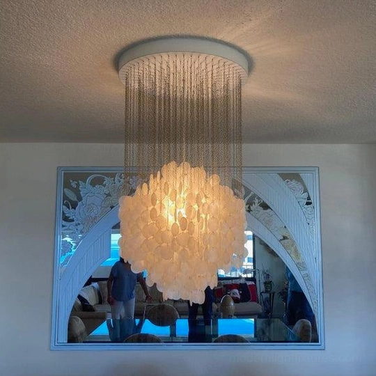 Warm-lit capiz shell chandelier in luxury living room with beige shell clusters and metal fringe suspension