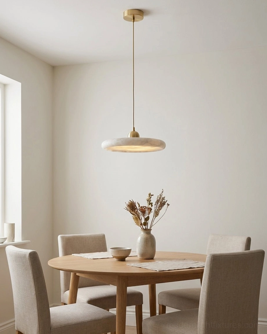 Lydia alabaster pendant lamp suspended above wooden dining table with warm neutral interior, soft ambient downward lighting