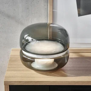 Modern Macaron table lamp three-quarter side view on wooden side table showing smoke gray glass and warm diffused lighting in interior setting