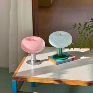 Pink and mint green macaron table lamps displayed on home side table with book and plant