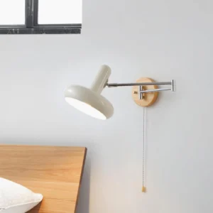 Maddie swing arm wall sconce displayed in bedroom setting with wooden bedside table and dark window frame, showing wood color and chrome finish options