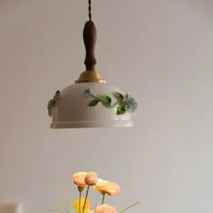 Maelis ceramic pendant light with brass hardware and wooden stem, oblique angle showing botanical hand-painted details and warm brass accents