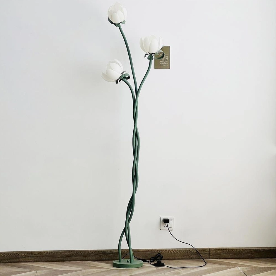Magnolia flower floor lamp with green stem and white acrylic blooms positioned beside furniture with product identification tag