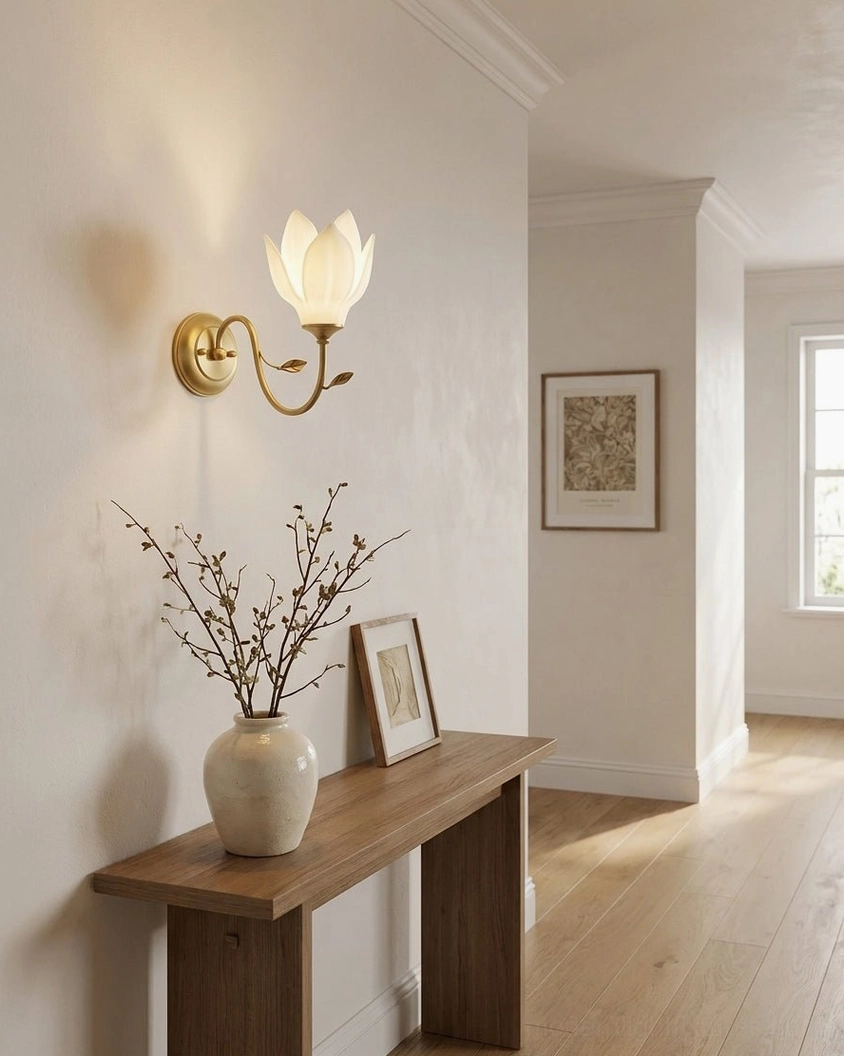 Magnolia wall sconce installed above wooden entryway console with warm ambient uplight illumination