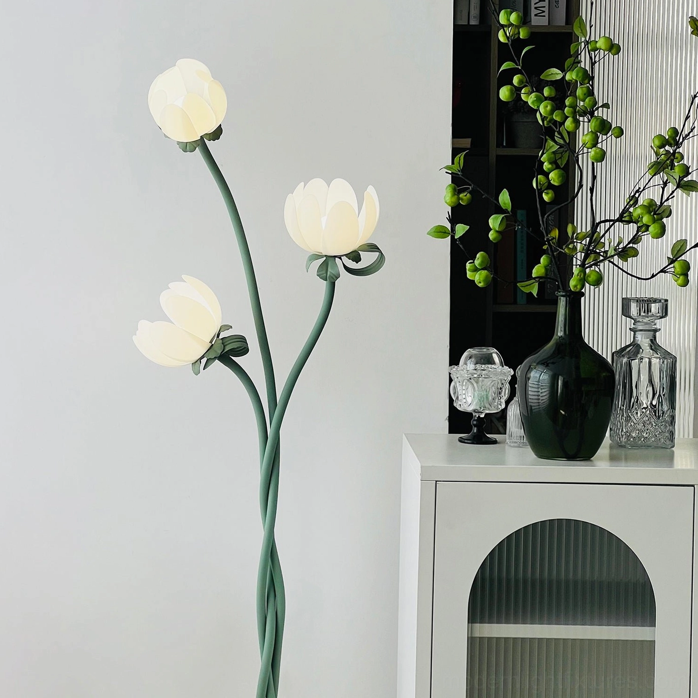 Magnolia bud floor lamp with illuminated white acrylic flower shades casting soft glow in room with white cabinet display