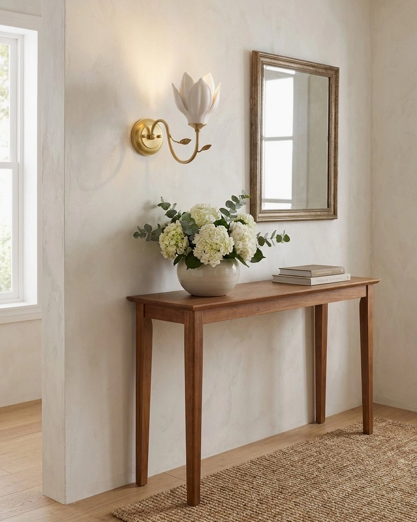 Magnolia ceramic wall sconce in hallway above wooden console with potted flowers and mirror decor