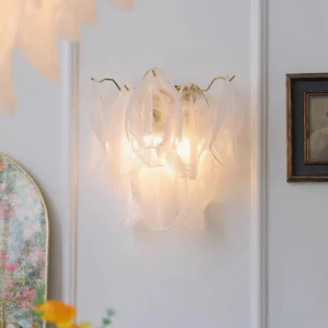 Magnolia wall sconce installed on paneled wall with framed artwork and floral décor, showing warm ambient lighting effect