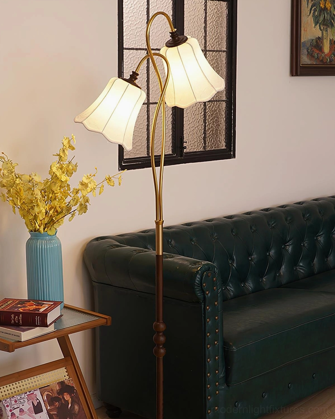 Magnolya dual-head floor lamp living room three-quarter side view, green sofa, warm metal pole decorative details ambient lighting