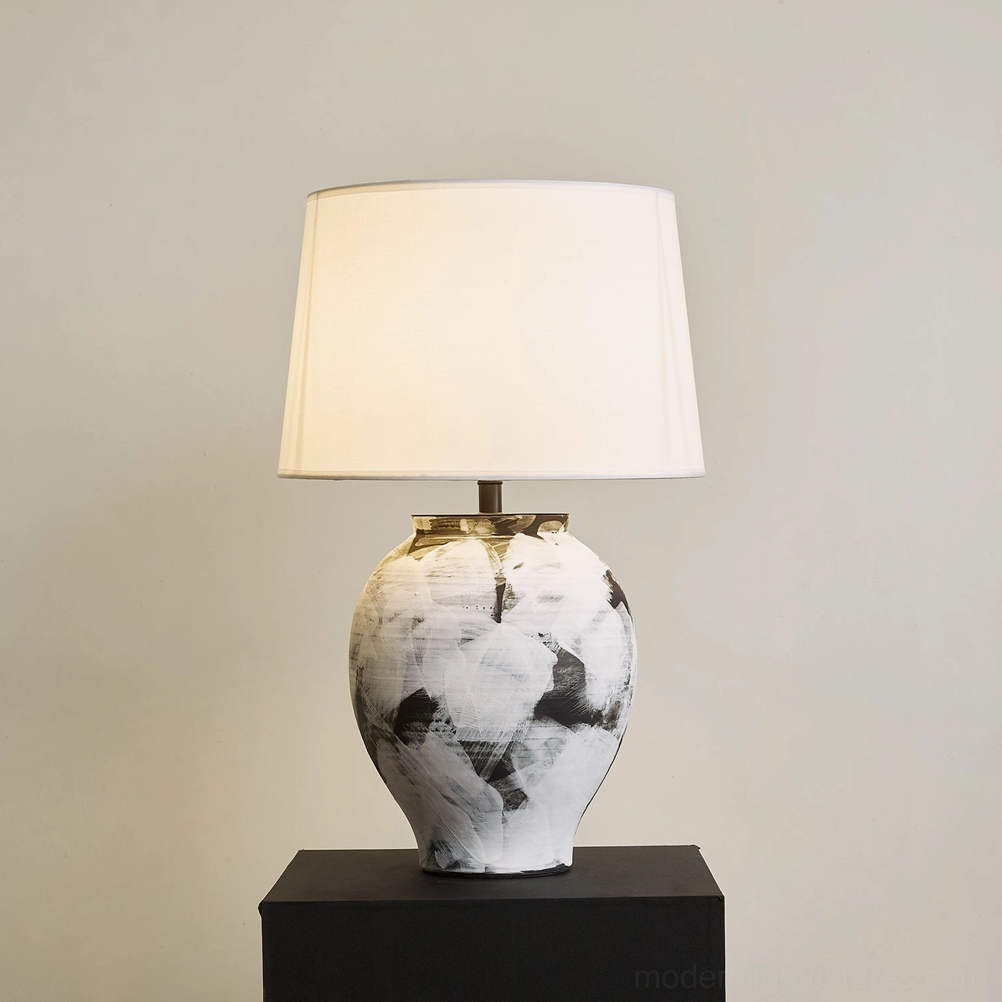 Malta ceramic table lamp illuminated showing warm light glow through white fabric shade and abstract painted base