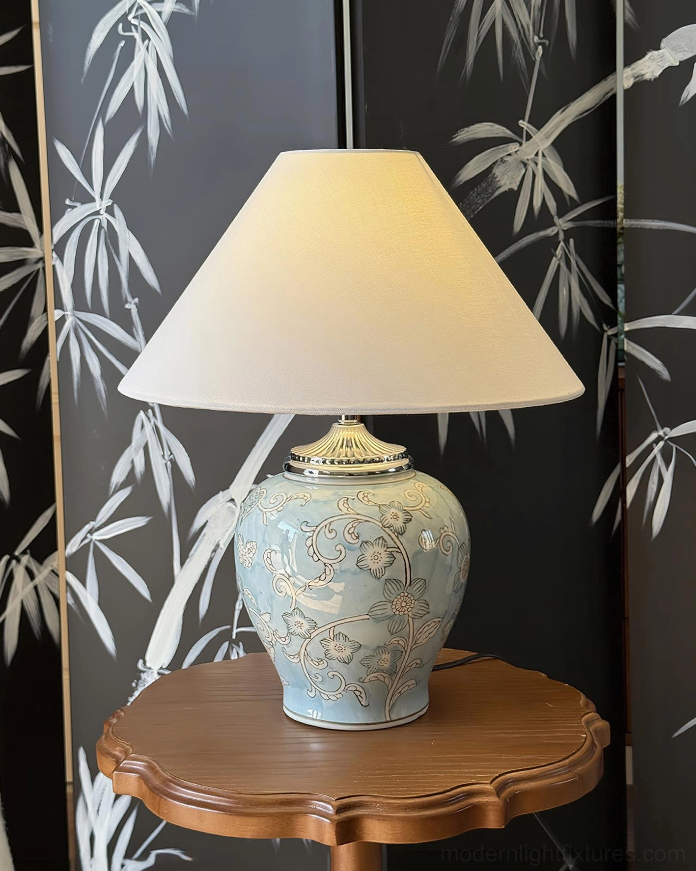 Pale blue embossed floral ceramic table lamp with vine patterns and white tapered fabric shade on wooden side table, minimalist bedroom styling with bamboo screen backdrop