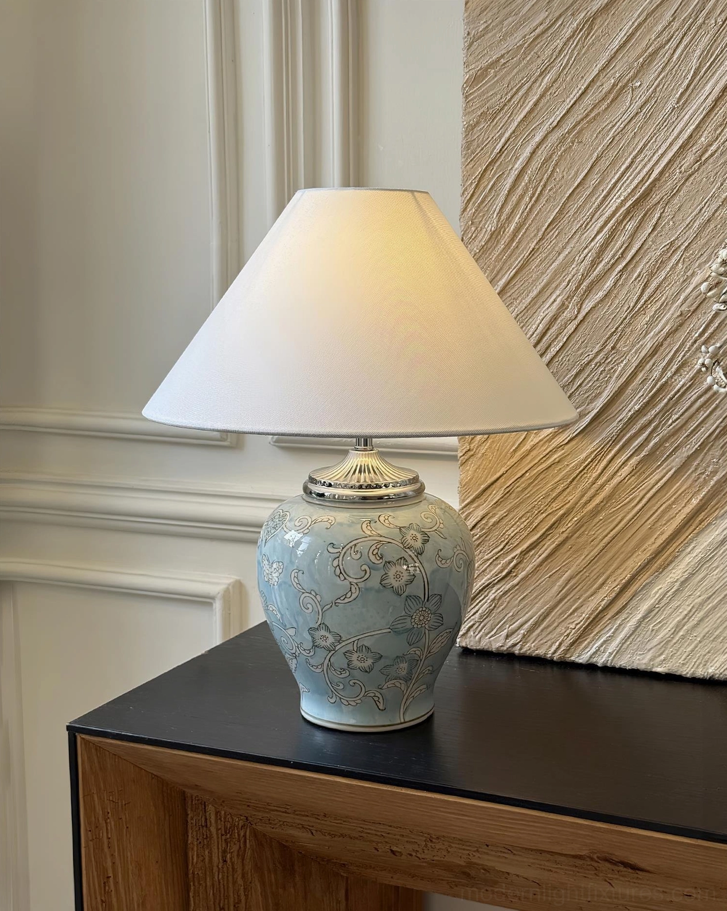 Light blue floral ceramic table lamp with delicate botanical patterns and off-white tapered shade displayed on entryway console table in minimalist neutral interior design space
