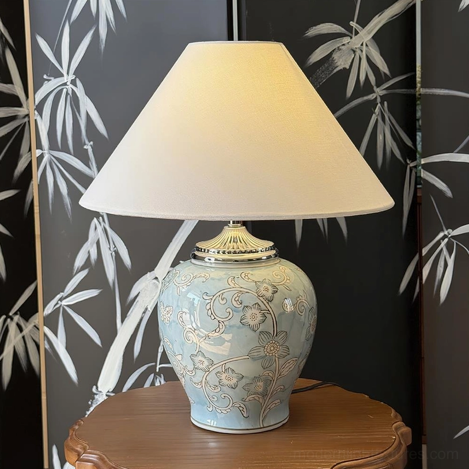 Cobalt blue ceramic table lamp with decorative floral motifs and off-white fabric shade, displaying rich glaze depth and artistic hand-painted botanical design elements