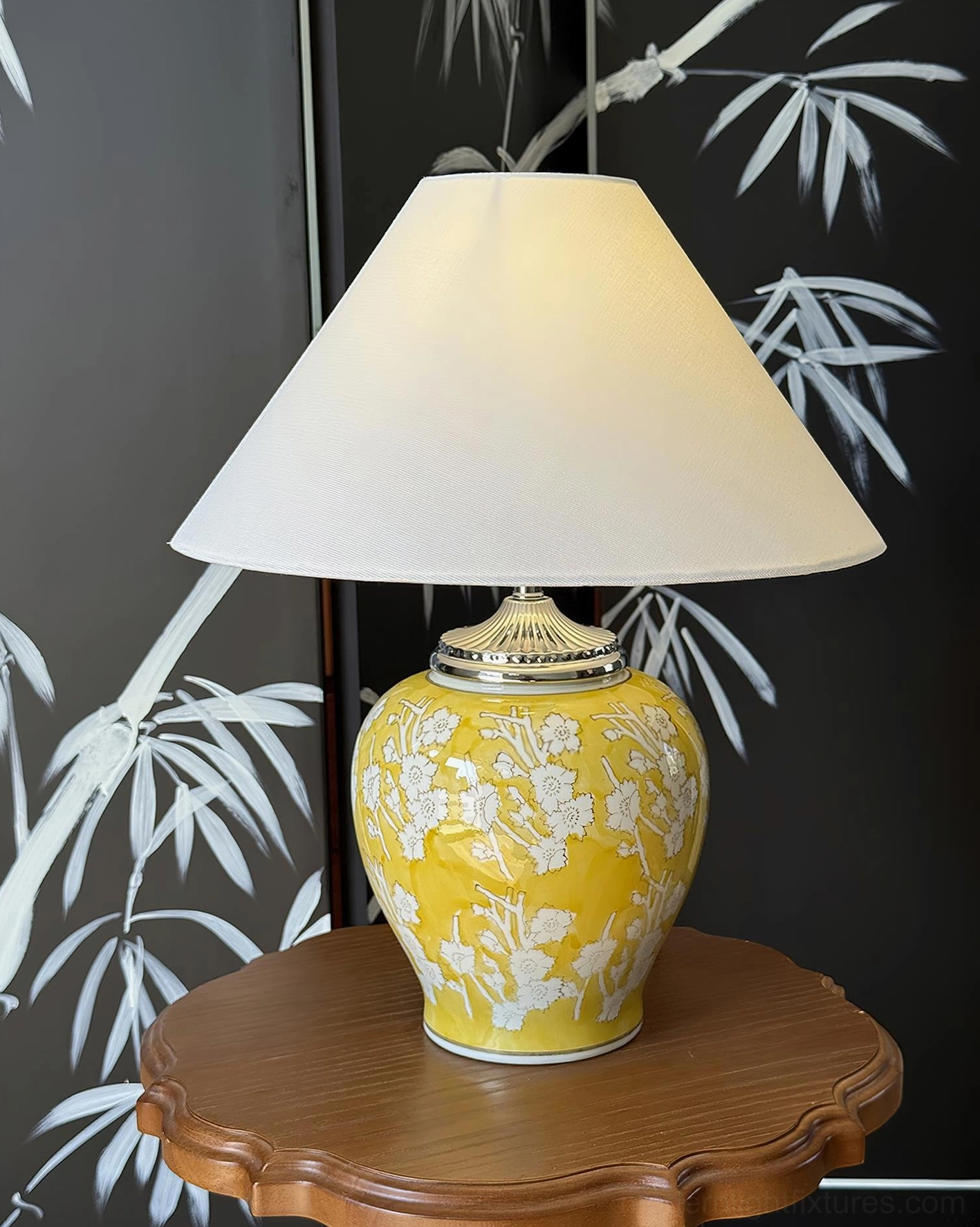 Yellow glazed ceramic table lamp with delicate white flower patterns displayed on wooden side table against bamboo folding screen, styling with traditional Asian interior elements