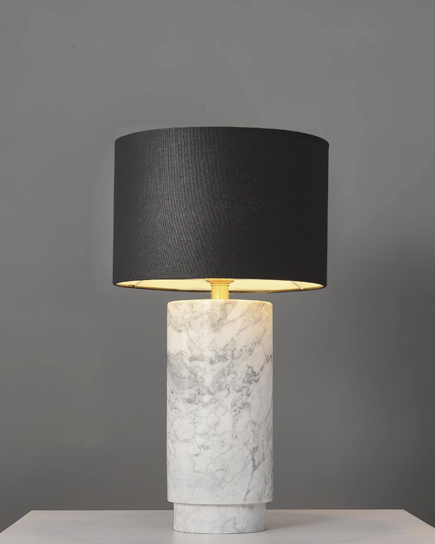 Sculptural marble table lamp with black fabric shade and white veined cylindrical base in minimalist studio lighting setup