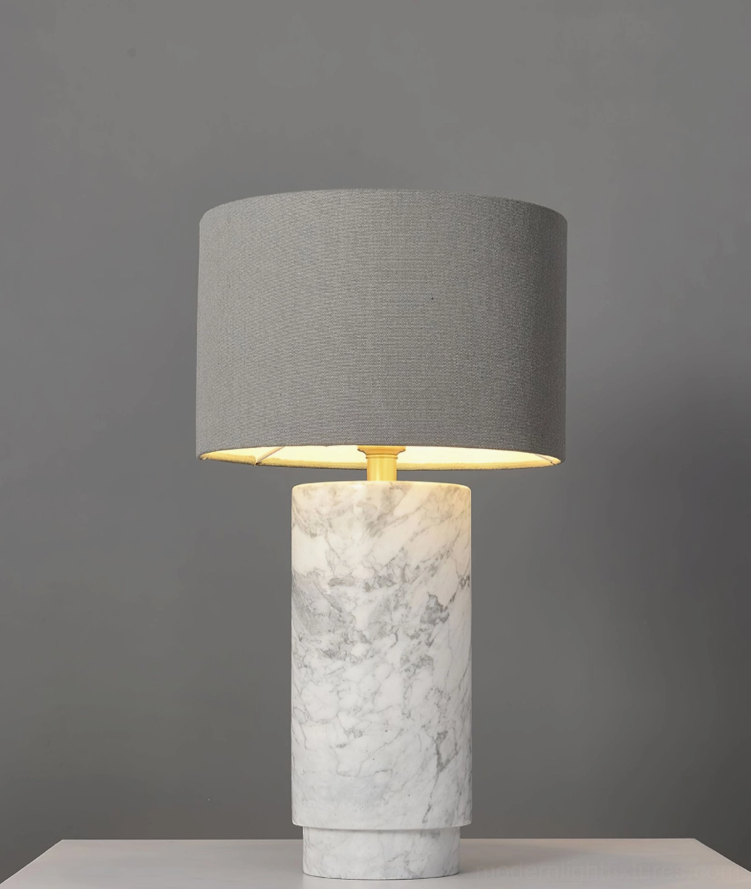 Cylindrical marble table lamp with grey fabric shade and minimalist modern design against grey background studio shot